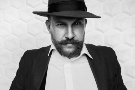 A portrait of a stylish elegant man posing in red suit and hat on the studio over the white background. Men's beauty, fashion, style.の写真素材