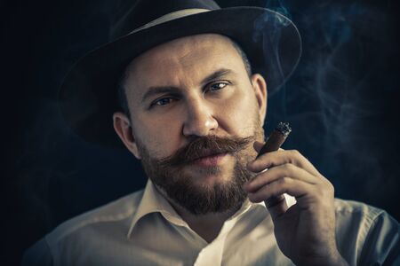 A close up portrait of a thoughtful man with a cigar posing in the studio over the black background. Men's beauty, fashion, style.の写真素材