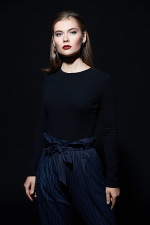 Beautiful elegant young woman posing at studio over black background.
