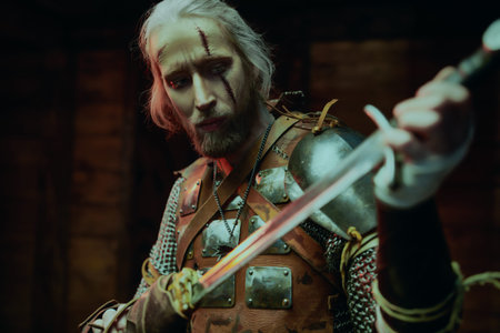Portrait of a brave medieval warrior in armor looking at his sword. The Witcher man.