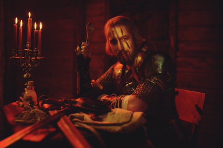 A medieval warrior in armor and with weapons is resting in the inn. Stage portrait. The Witcher man.