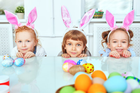 Easter holidays. Happy two girls and a boy with bunny ears prepare gifts for Easter. Loving family...