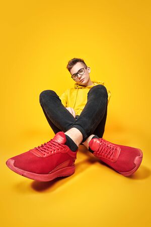 Cool young man in bright yellow hoody and glasses posing on a yellow background. Youth fashion.の写真素材