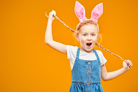Funny red-haired girl holds her pigtails and screams. Happy childhood. Easter holiday. Studio...