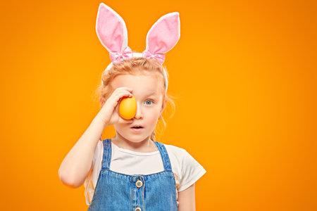 Cute red-haired girl holds a painted Easter egg and is surprised. Happy childhood. Easter holiday....
