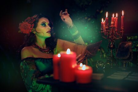 A beautiful red-haired sorceress conjures with a spell book and a magic crystal ball. Charming woman witch. Magic for Halloween.の写真素材