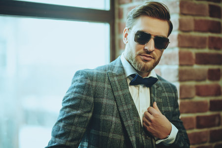 Handsome man in elegant checkered suit and sunglasses in a modern loft interior. Luxurious...