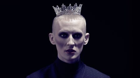 Portrait of a young man with womens makeup and with a crown on his head on a black background. Avant-garde fashion.の写真素材