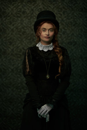 Beautiful Victorian woman in black dress and top hat stands in vintage interior. Steampunk.