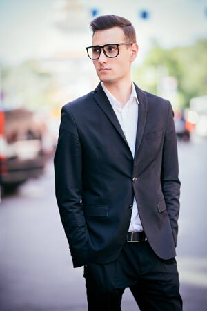 Portrait of a goodlooking young man walking along the street of a big city. Young businessman. Men's beauty, fashion.の写真素材