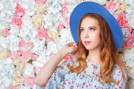 A portrait of a happy romantic girl in a hat posing in the studio over the background with flowers. Summer casual fashion, beauty.の写真素材