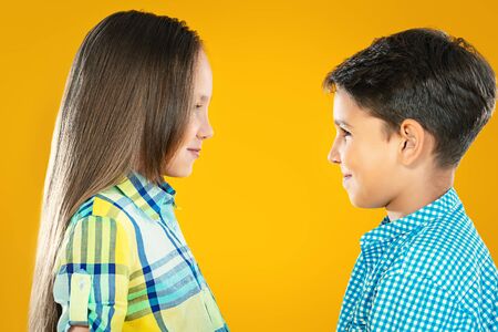 Two cheerful kids a boy and a girl are looking to each other and smiling. Studio shot on a yellow background. Beauty, summer, fashion, emotions.の写真素材