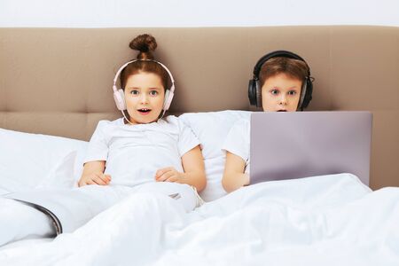 COVID-19 and home isolation. Funny kids relax and play in the children's bedroom with headphones and a laptop.の写真素材