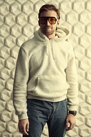 Portrait of a cool young man in white hoody and stylish yellow sunglasses. Youth style, men's fashion.の写真素材