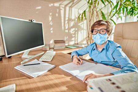 Coronavirus and life. Boy schoolboy student in a medical mask stays home at distance learning due to quarantine because of COVID-19.の写真素材
