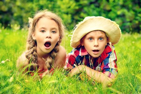 Happy children a boy and a girl are lying on a grass and are surprised. Sunny summer day. Happy holidays. Kid's fashion.の写真素材