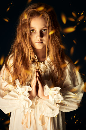 Scary little girl ghost in a white nightgown folded her hands in prayer. Black background. Halloween. の写真素材