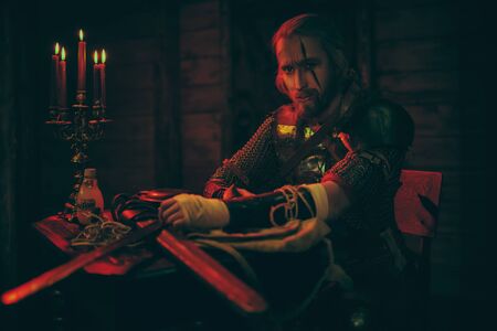 An experienced medieval warrior in armor and with a sword in a wooden house. Stage portrait. The Witcher man.の写真素材