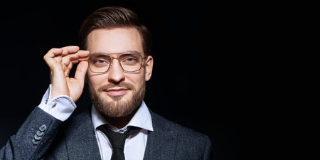 Handsome man wearing elegant suit and glasses smiling at camera. Businessman portrait on a black...