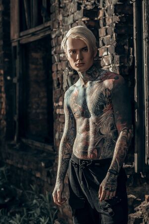 COVID-19 pandemic virus infection worldwide. A brutal young man with tattoo on his body stands on the background of a destroyed city.の写真素材