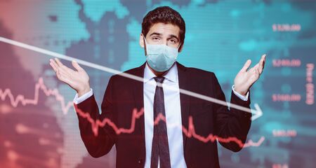 Coronavirus and business. A businessman in a medical mask makes a helpless gesture against the background of a coronavirus and stock charts.の写真素材