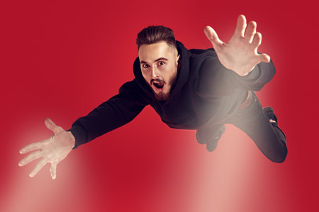 Excited young man is flying through the air. Studio portrait on a red background.