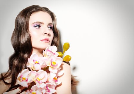Beauty woman. Portrait of a dreamy beautiful young woman with orchid flowers. Make-up and cosmetics. Beauty and health care.の写真素材