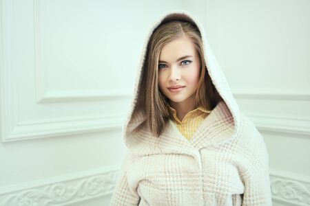 Pretty blonde girl in a light coat in a white interior. Spring and autumn clothes fashion.の写真素材