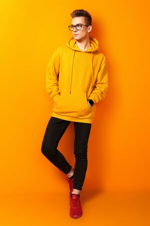 Cool young man in bright yellow hoody and glasses posing on a yellow background. Youth fashion.の写真素材