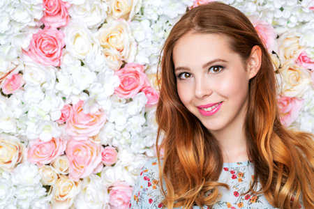 A portrait of a happy romantic girl smiling in the studio over the background with flowers. Summer casual fashion, beauty.の写真素材