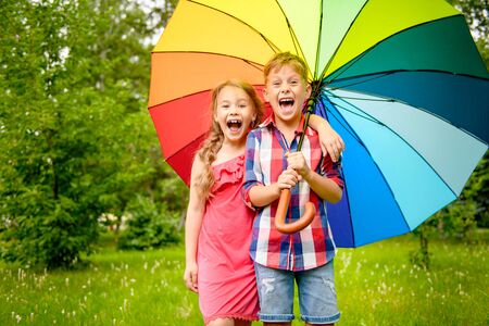 Portrait of a happy little children holding a multicolored umbrella in their hands and joyfully shouting in the Park. Summer holidays. Children's fashion.の写真素材