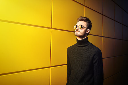 Urban style. Portrait of a stylish young man in black pullover and round mirror sunglasses posing on...