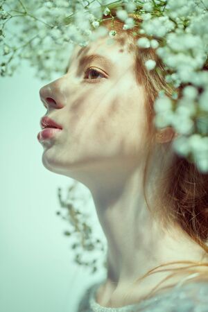 Beautiful young girl with lovely freckles on her face and in a gypsophila wreath on a white background. Inspiration of spring and summer. Perfume, cosmetics concept.の写真素材