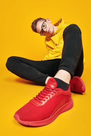 Cool young man in bright yellow hoody and glasses posing on a yellow background. Youth fashion.の写真素材