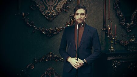 Stylish young man in elegant classic suit stands with a walking stick in a luxurious vintage interior. Men's fashion.の写真素材