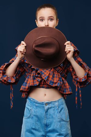 Fashion shot. Portrait of a pretty emotional girl model posing in jeans, checkered blouse and brown hat. Country, western style. New summer collection.の写真素材