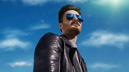 Handsome young man in a black leather jacket and sunglasses stands outdoor against the blue sky. The...