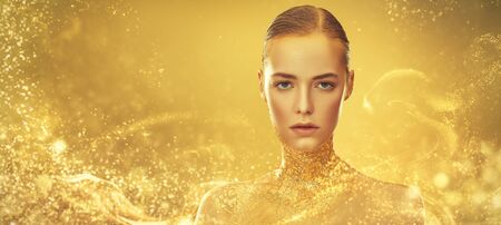 Beauty, fashion gold concept. Portrait of a beautiful girl model with golden skin and golden make-up on a sparkling background with golden lights. Jewelry. Cosmetics and beauty care. Copy space.の写真素材