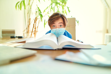 Coronavirus and education. Tired unhappy boy schoolboy student in a medical mask stays home at...