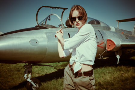 Portrait of a beautiful pilot girl standing next to her fighter plane at the airfield.