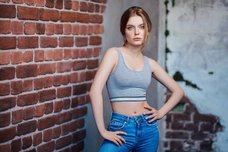 Portrait of a beautiful slim girl in jeans and a sports top against a brick wall. Active lifestyle. Beauty, fashion.の写真素材