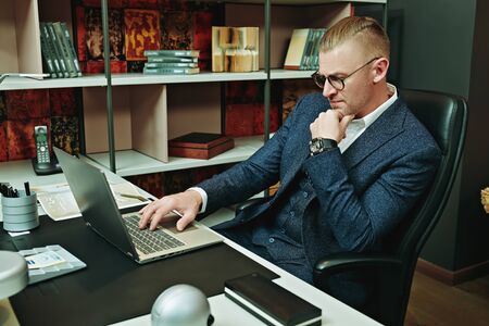 Respectable middle-aged businessman in a suit and glasses works in a modern office. Successful manager concept.の写真素材