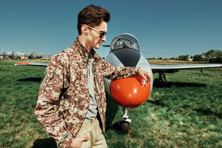 Handsome man pilot wearing military uniform stands by his fighter jet at the airfield. Military...
