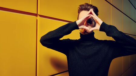 Urban style. Portrait of a stylish young man in black pullover and round mirror sunglasses posing on a street by the yellow industrial wall. Male fashion. Copy space.の写真素材