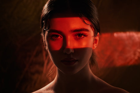 Portrait of a beautiful girl with shiny make-up and red arrows on her eyes in red light. Make-up and...