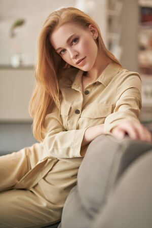 Portrait of a beautiful blonde girl having a rest on a sofa in her cozy living room. Happy life, happy people concept.の写真素材