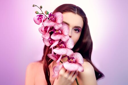 Beauty woman. Portrait of a beautiful smiling young woman with orchid flowers. Make-up and cosmetics. Beauty and health care.の写真素材