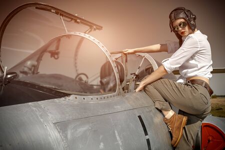 Portrait of a beautiful girl pilot wearing helmet and sunglasses sits in her fighter jet at the airfield. Military aircraft.の写真素材