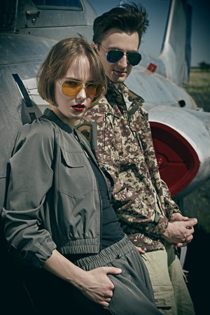 A beautiful girl and a handsome man pilots stand next to a fighter jet at the airfield. Military...