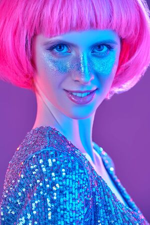 Beauty, makeup and cosmetics concept. Portrait of an attractive girl with shiny glitter freckles and a bright pink wig. Holiday and party style.の写真素材